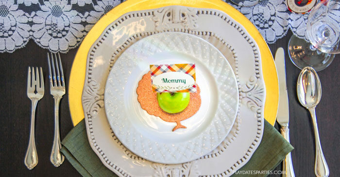 Vintage Thanksgiving decorations with a place setting that includes a gold charger, green cloth napkin, white plates and vintage style silverware.