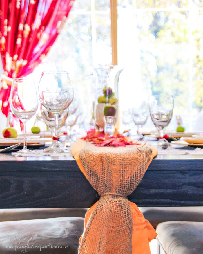 A gold tablecloth folded up as a table runner with a burlap ribbon and faux fall leaves on top for a vintage feel.