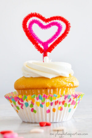 Vanilla cupcake with a heart shaped topper made out of pipe cleaners.