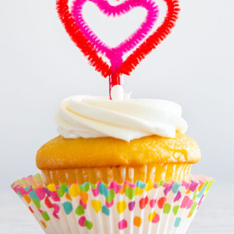 Vanilla cupcake with a heart shaped topper made out of pipe cleaners.