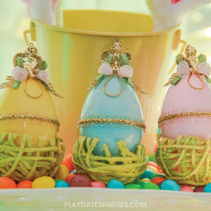 yellow pink and blue plastic eggs decorated Faberge style with gold trim, gold cherubs and fabric rosettes