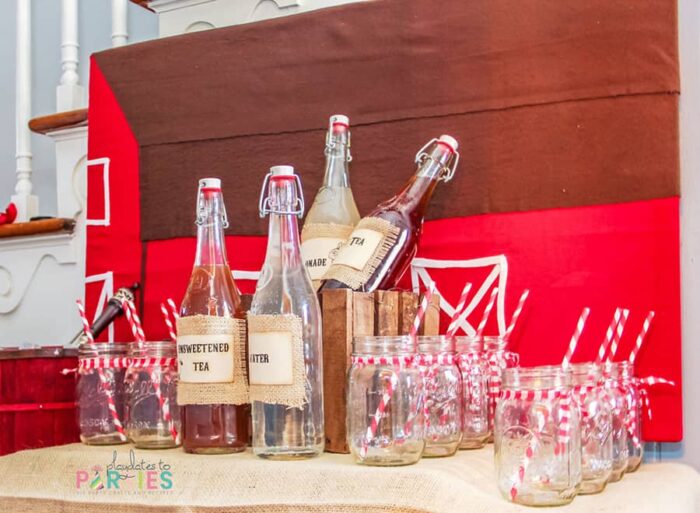 a drink buffet with a backdrop that looks like a red barn, mason jars with red paper straws and red gingham tied around the openings