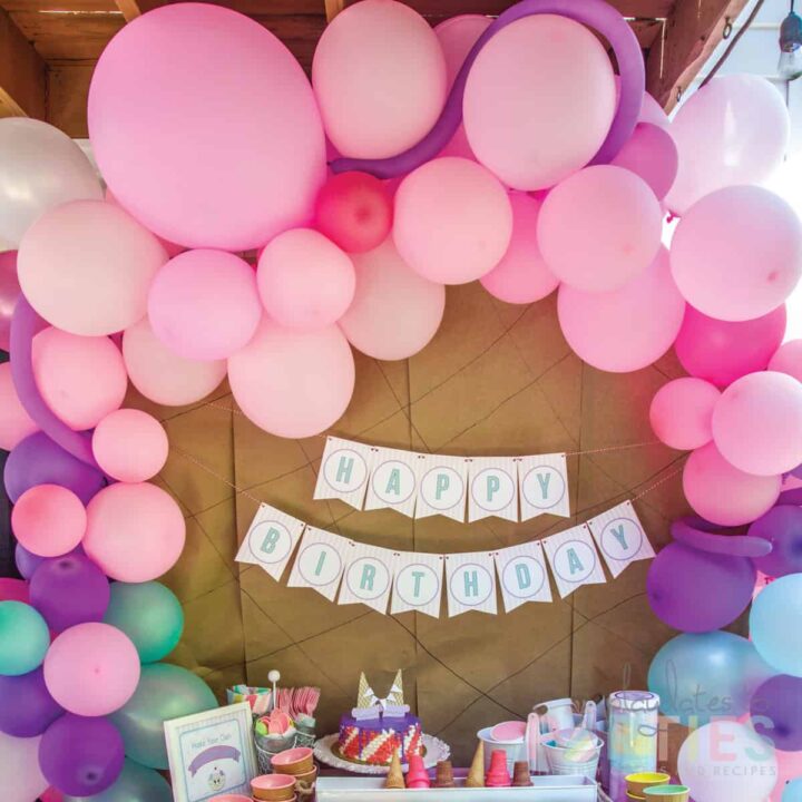 pink purple and teal balloons arched over a party table