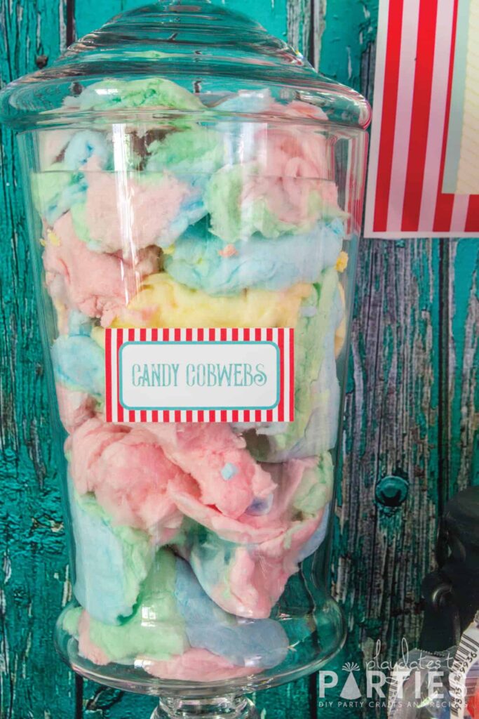 Apothecary jar filled with colorful cotton candy and a tag that says candy cobwebs