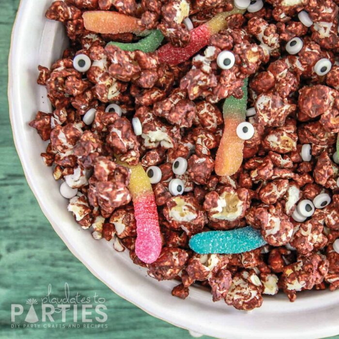 close up of chocolate coated popcorn with googly eye candy and gummy worms
