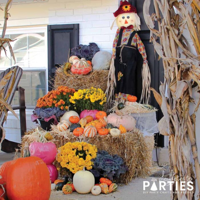 A front porch with a large display of hay bales, fall flowers, gourds, decorative lettuces, corn stalks and scarecrows