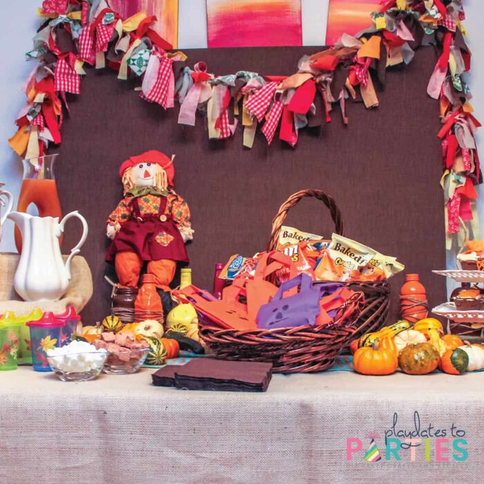 a party table with a rag garland, jack o lantern bags, scarecrows, pumkins, and fall leaf decorations