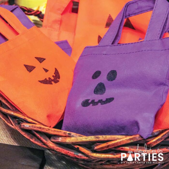 Orange and purple mini fabric bags with jack-o-lantern faces drawn on them