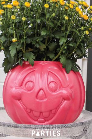 Pink painted plastic jack o lantern with a happy face and yellow chrysanthemum blooming out the top