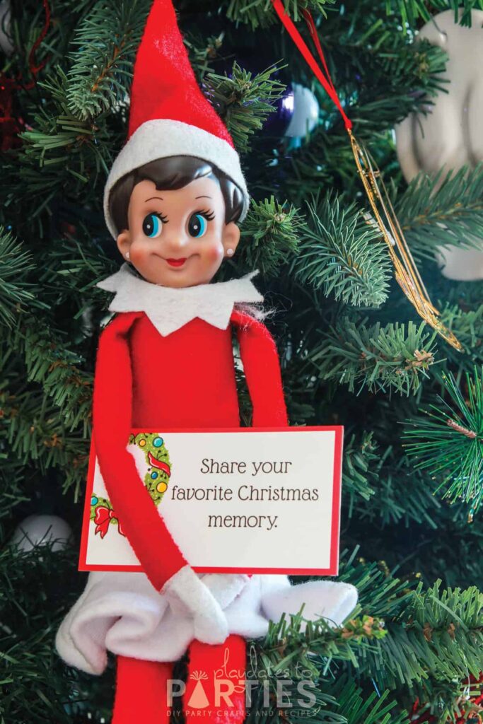 elf sitting in a Christmas tree holding a card that says share your favorite Christmas memory