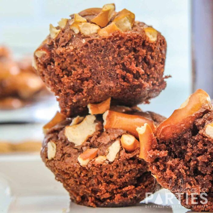 close up image of two brownies stacked together on a white plate in front of a bowl of pretzels