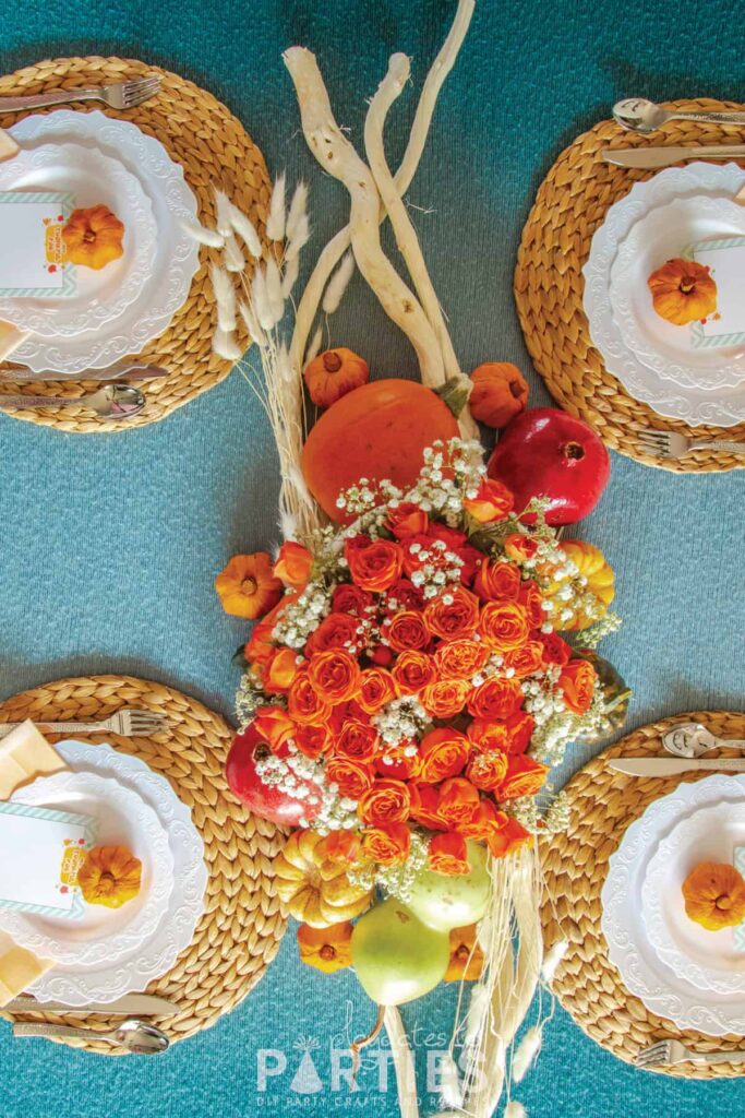 top view of a Thanksgiving table with orange roses, white plates and a blue tablecloth