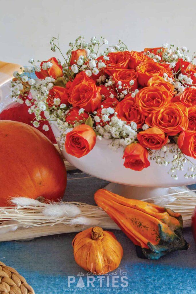 orange miniature roses with baby's breath in a white pedestal bowl on a blue tablecloth