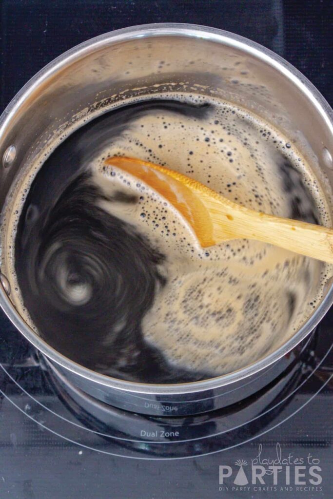 Beer syrup cooking in a pot and being stirred with a wooden spoon