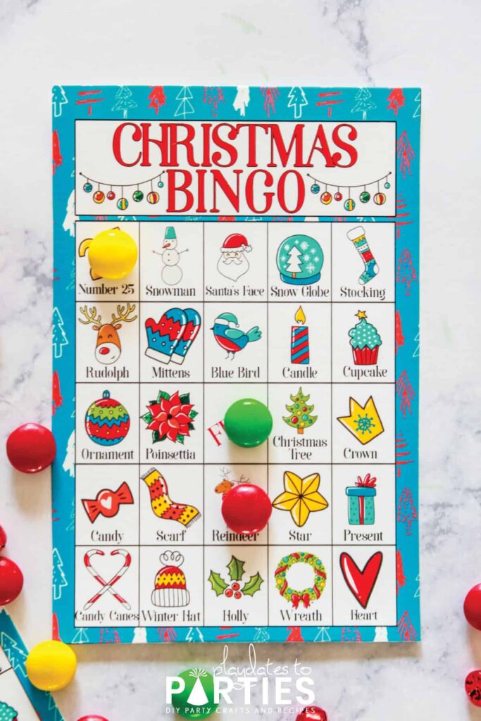 a brightly colored Christmas Bingo card on a table with three spots marked by candy