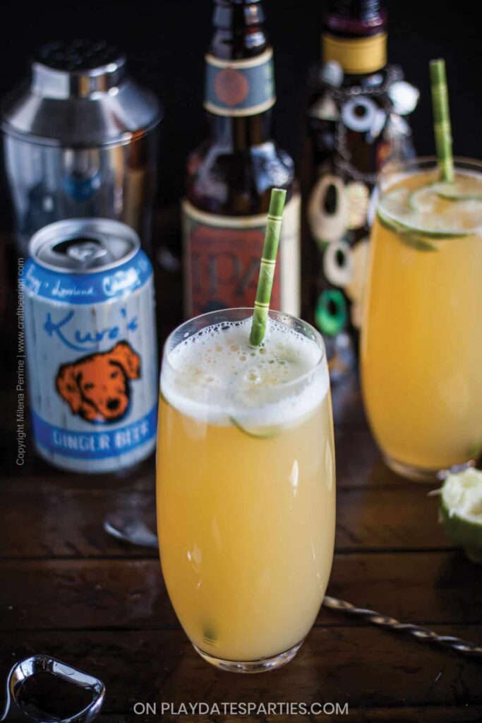a tall glass on a dark wood table filled with a beer cocktail and a bamboo straw sticking out of the top
