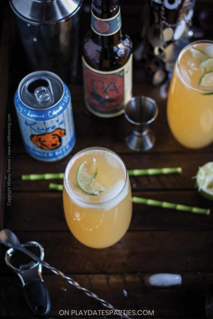 Overhead view of a beer cocktail on a dark wood table with bamboo stir sticks and open beer containers