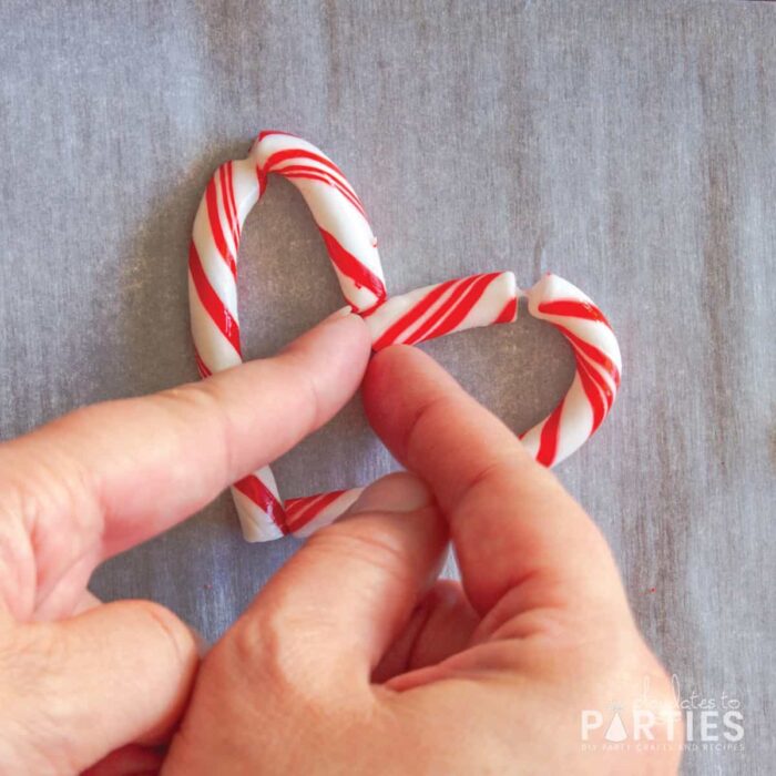 pinching together the ends of the candy cane to create a closed heart