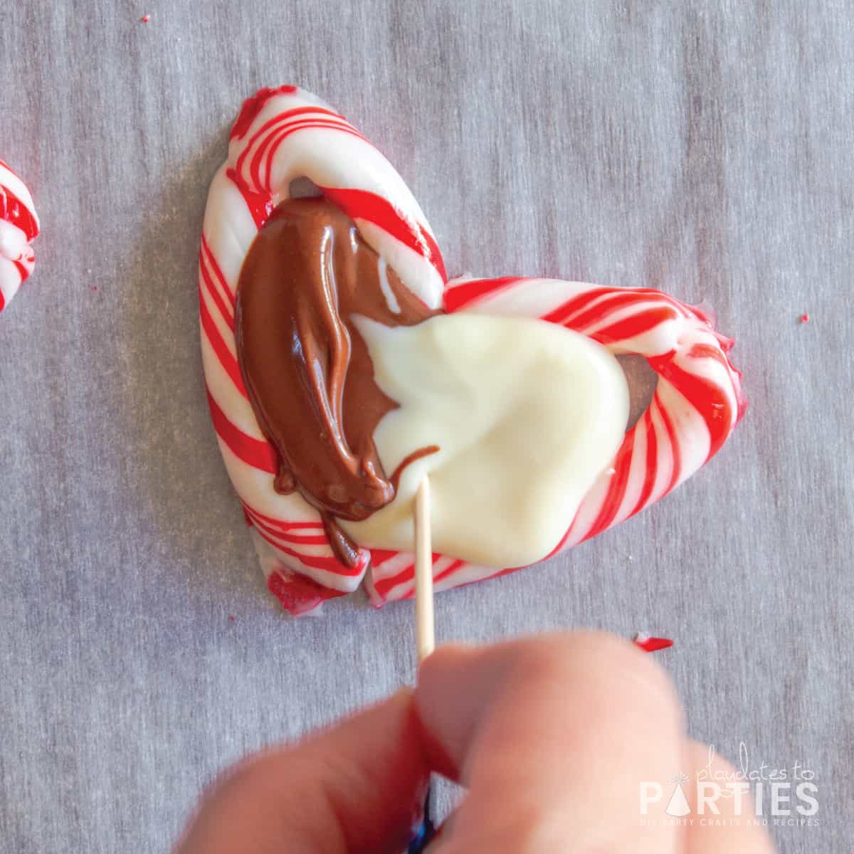 A woman's hand swirling melted white and milk chocolate in a candy cane heart.