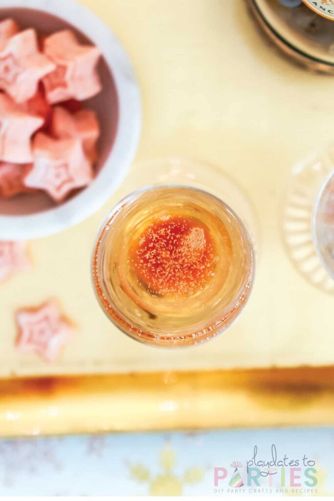 Top view of champagne bubbling in a flute next to a bowl of star-shaped pink sugar cubes