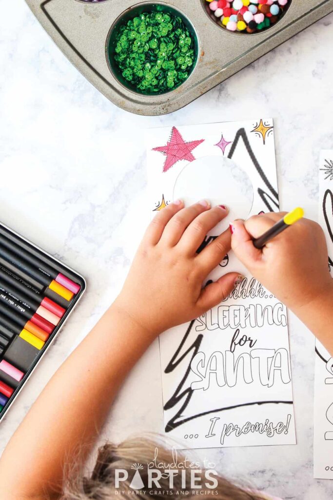 Image of a child coloring in a Christmas door hanger with colored pencils and a tray of supplies nearby