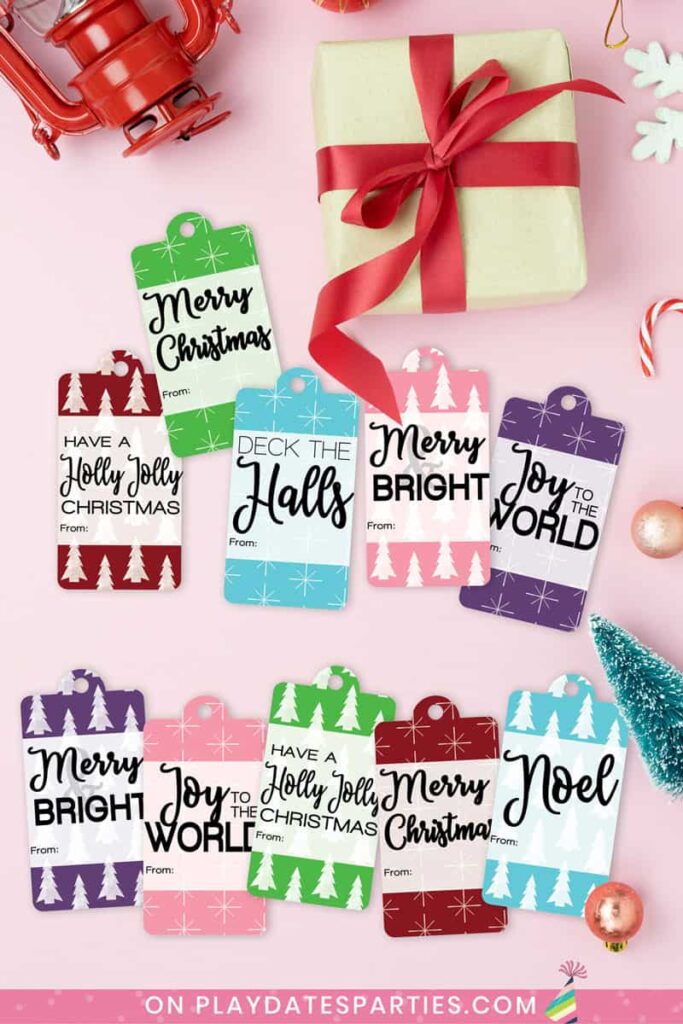 printable Christmas gift tags in assorted colors on a pink table surrounded by holiday paraphernalia