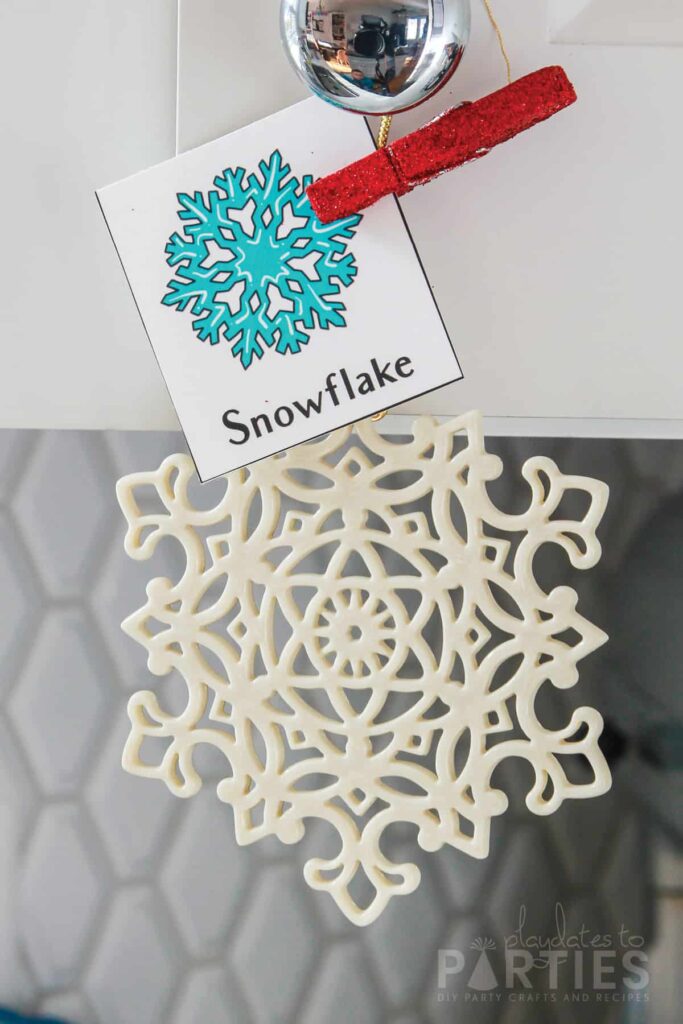 snowflake shaped Christmas ornament hanging from a cabinet with a card clipped to it that says snowflake