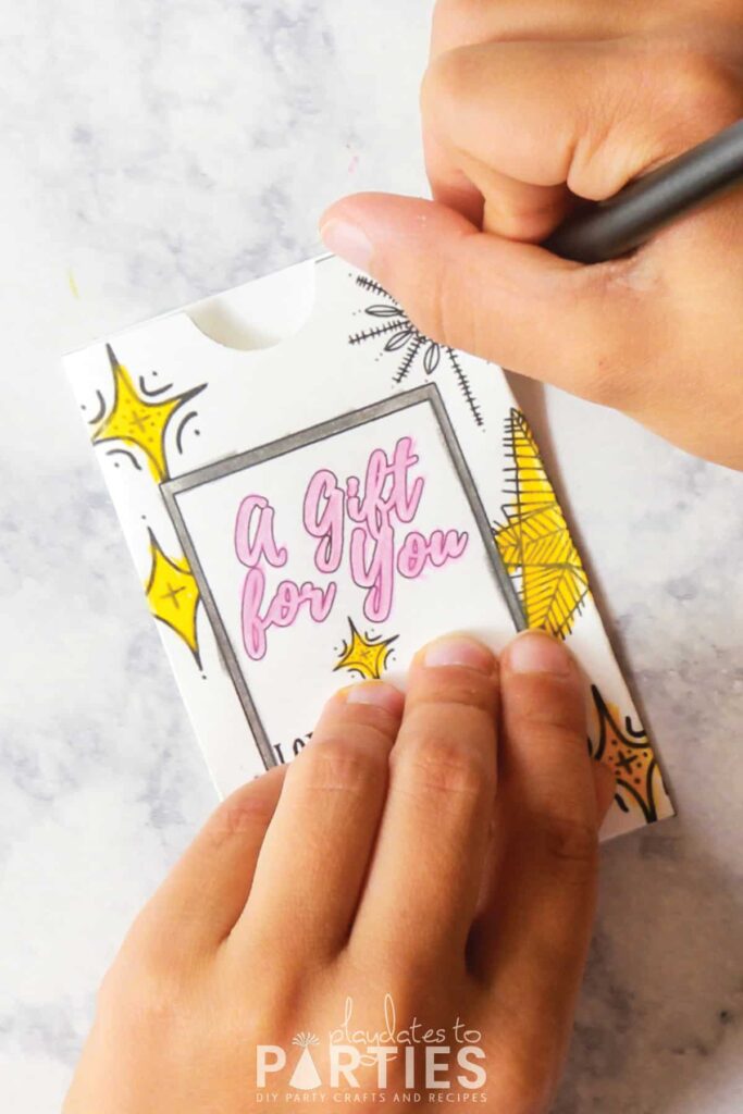 A child's hands coloring in the stars on a personalized gift card holder