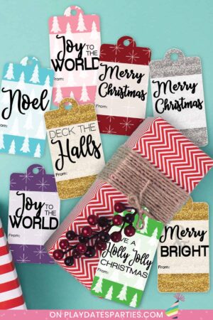 a variety of holiday gift tags on a blue table surrounding a present wrapped in red paper tied with brown twine