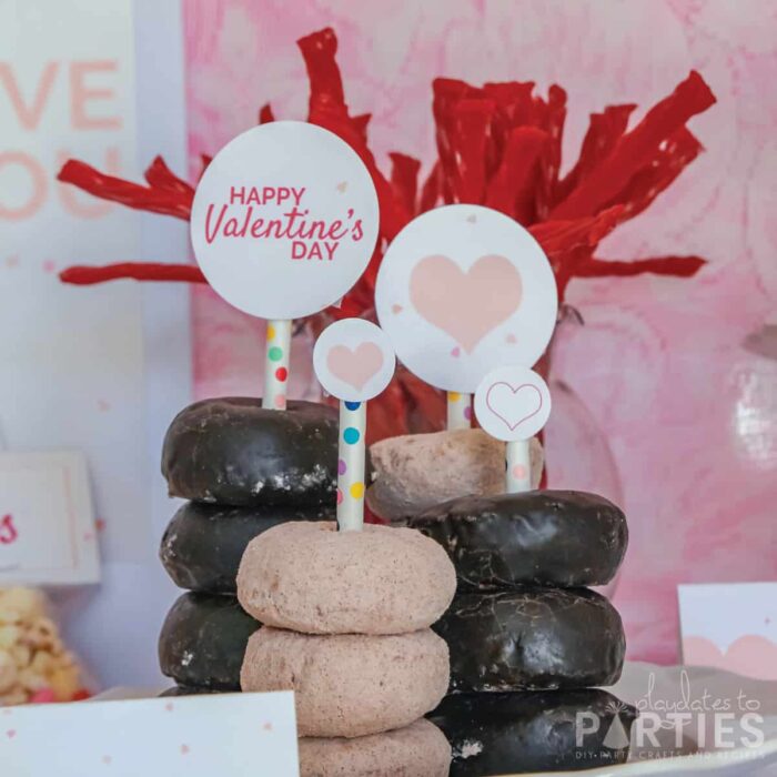 mini donuts stacked on a plate, with a paper straw through the center. The paper straws have decorative party circles glued to the top.