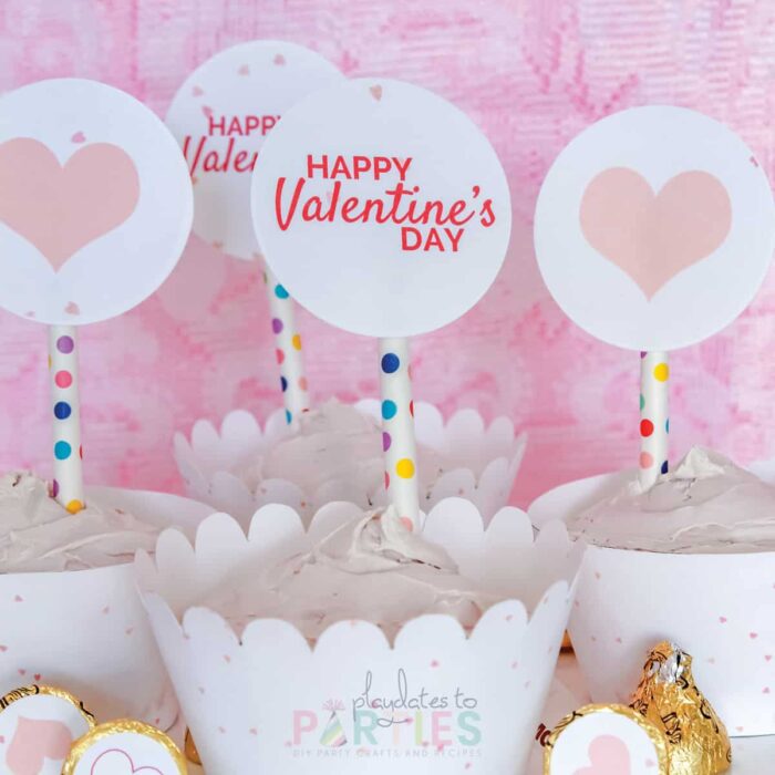 close up of cupcakes with printed wrappers and circles that have pink hearts and say Happy Valentine's Day