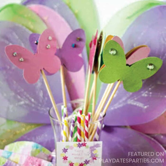 close up of purple, green, and pink butterfly wings with coordinating buttterfly wands in a vase in front.