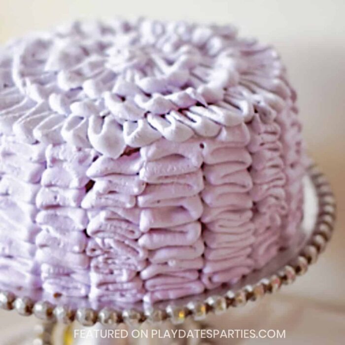 cake on a silver cake plate piped with purple frosting ruffles