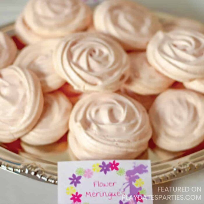 light pink meringue cookies piped to look like flowers on a silver platter with a label in front that has a fairy and flowers