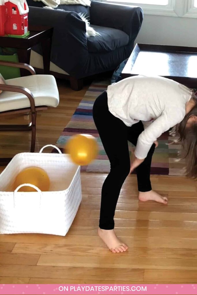 a young kid tossing a balloon into a white basket that's behind her.