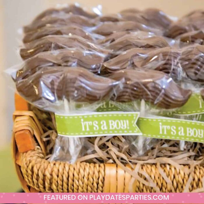 mustache lollipop favors in a basket with a green tag that says It's a Boy