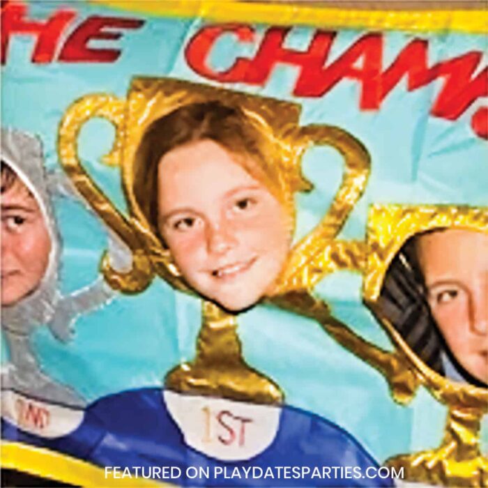 kids with faces in a photo prop that looks like trophies with words the champs across the top