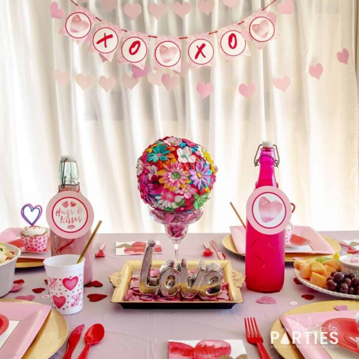 dining table decorated for Valentine's Day lunch with disposable plates and a centerpiece made with a margarita glass and a flower-covered pom