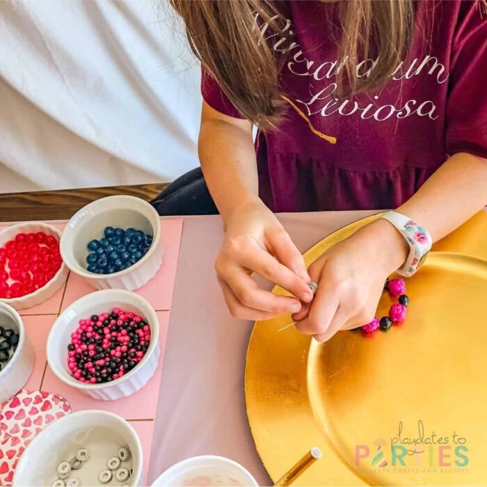 young girl threading beads on string to make a bracelet with small bowls of beads nearby