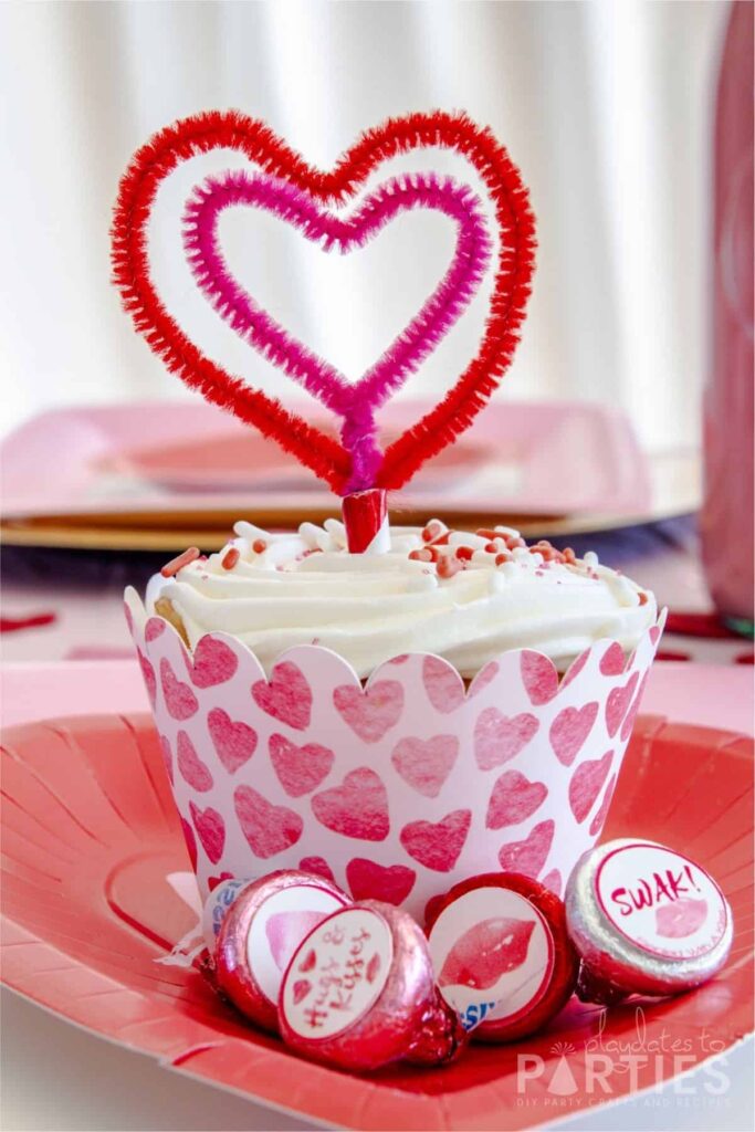 close up of a cupcake in a custom wrapper with a heart shaped topper and Hershey's kisses decorated with Valentine's Day labels