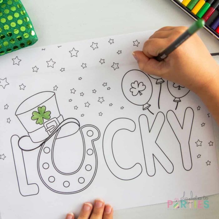 child's hand coloring a sheet that says lucky with a leprechaun hat and St. Patrick's Day balloons