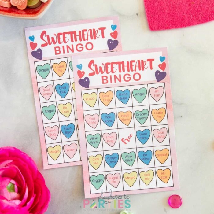 two Sweetheart bingo cards on a marble table surrounded by candy, flowers, and decorative hearts