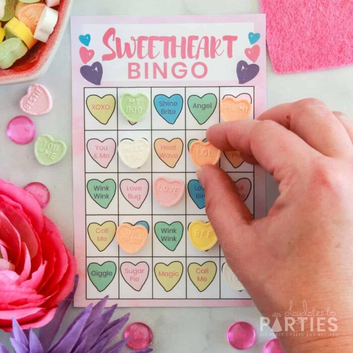 woman's hand placing a conversation heart candy on a bingo card for Valentine's Day