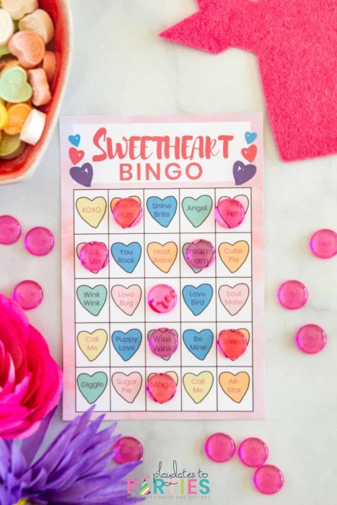 a pink bingo card with pictures of hearts and translucent pink acrylic confetti used as markers