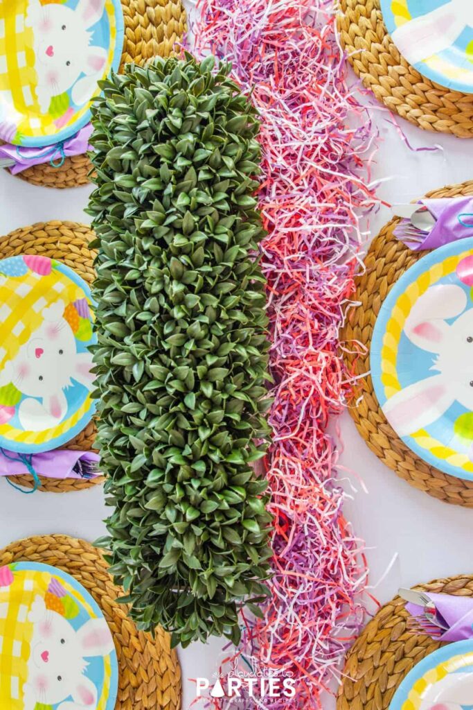 Overhead view of a dining table decorated for Easter with greenery and paper Easter grass