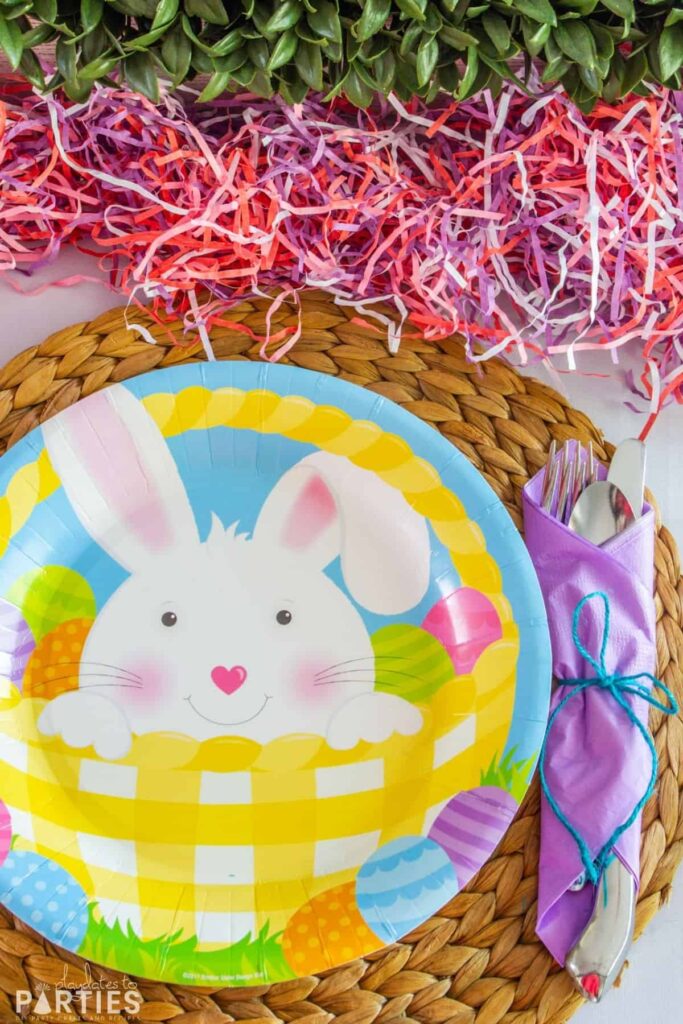 close up of an Easter plate on a woven placemat with utensils wrapped in a purple paper napkin