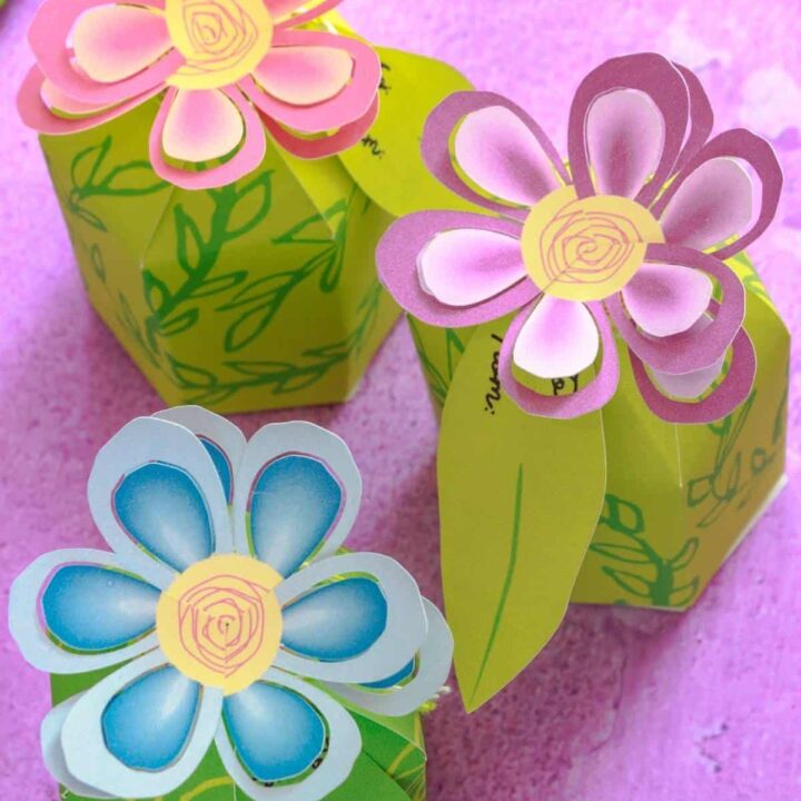 DIY flower favor boxes on a purple surface with flowers in pink, purple, and blue