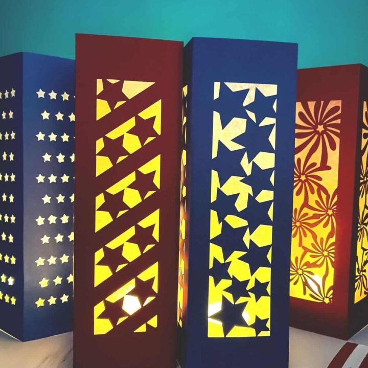 Four patriotic paper lanterns - three with stars designs, and one with fireworks - all glowing in a dark room