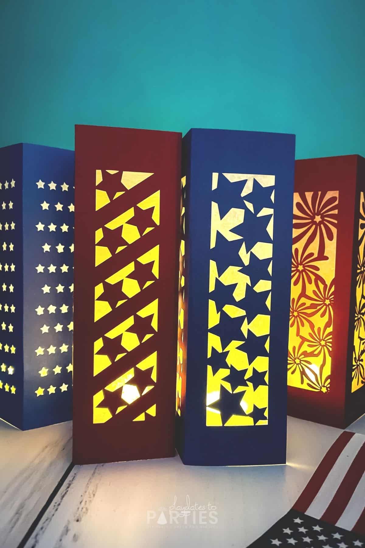 Four patriotic paper lanterns - three with stars designs, and one with fireworks - all glowing in a dark room