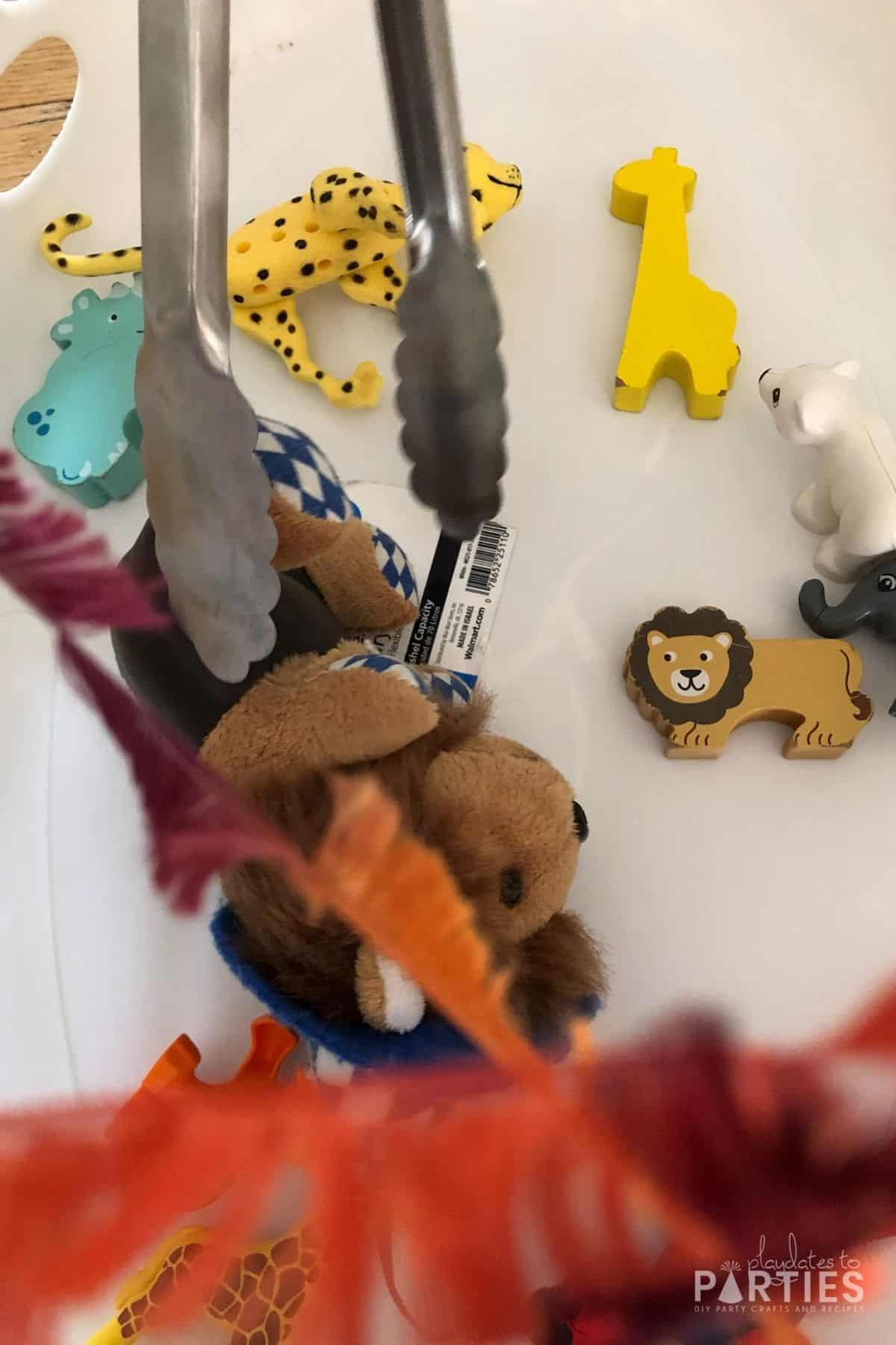 close up of kitchen tongs reaching to grab a stuffed lion